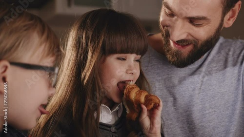 Close up of the cute funny small kids with their father eating a croissant with a chocolate and smiling. Portrait shot. Indoor photo