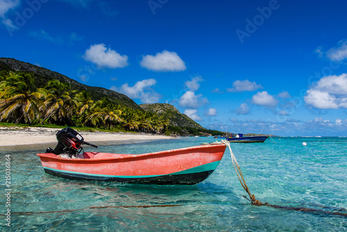 A red fishing boat is anchored in the transparent waters of the lagoon of Desirade Island, under a blue sky