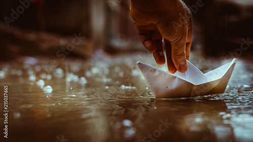 Obraz na płótnie Close up of hand playing with paper boat in water puddle