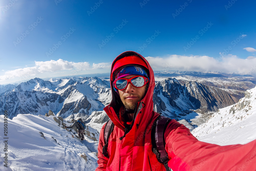 Selfi male mountaineer in snowy mountains, wearing a helmet with a backpack