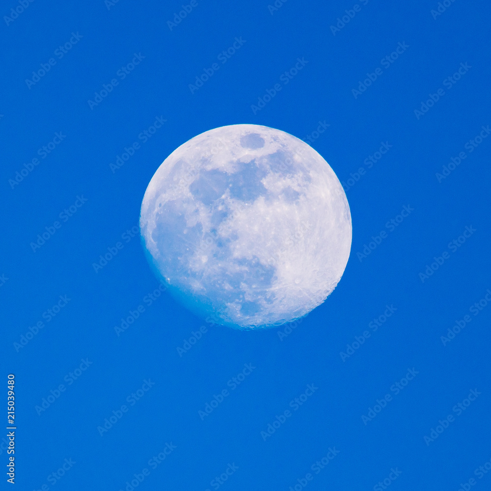 The moon shines against the blue sky