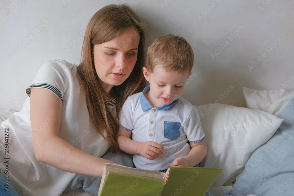 Family mom and son toddler read books laying on the bed. Family reading time. Family mom and son toddler read books laying on the bed. Family reading time.