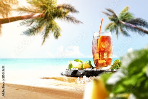 Fresh cold ice tea drink on table and landscape of beach with two palms. 
