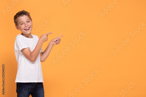 Young emotional little boy on orange studio background.