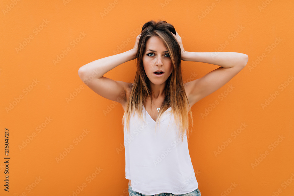 Portrait of beautiful woman with hands on head isolated on orange background Portrait of beautiful woman with hands on head isolated on orange background