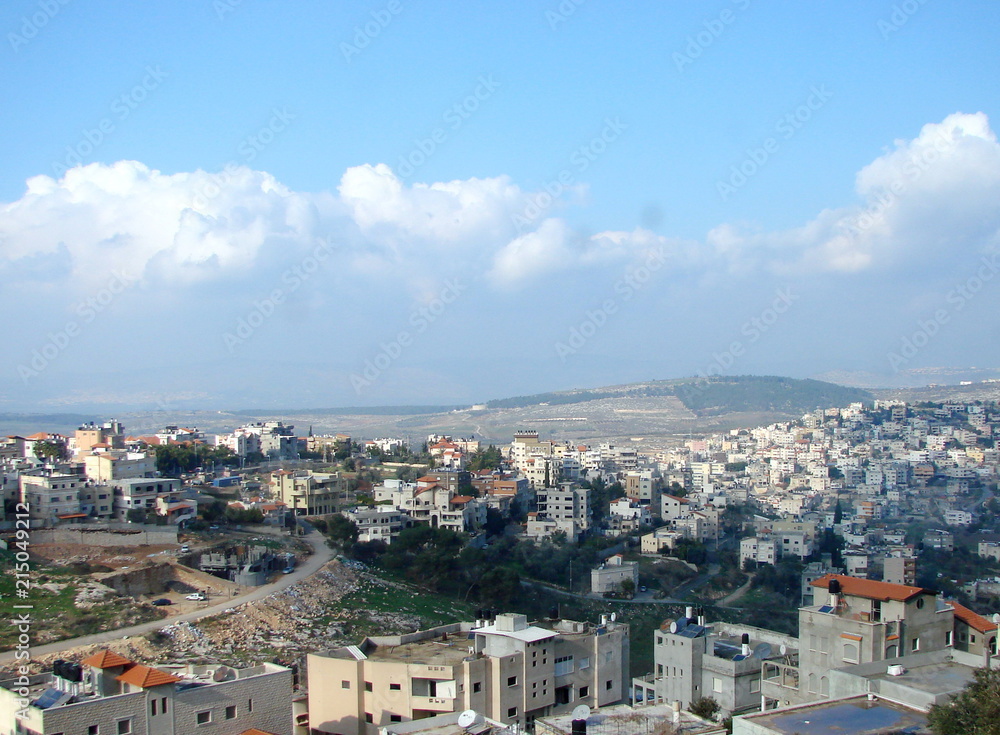 Panorama of cloudy blue sky above Nazareth city at the foot of the hills on the horizon.