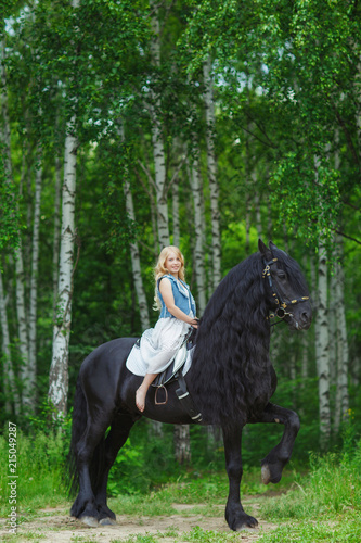 Little girl is riding a friesian horse, outdoor summer © Natalia Chircova