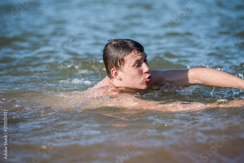 A boy teen swims in a spray of water - a concept of a beach holiday