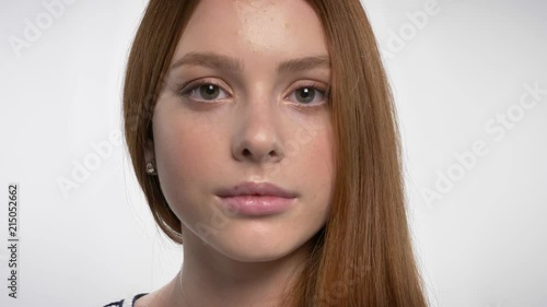 Face of young calm ginger girl is watching at camera, white background