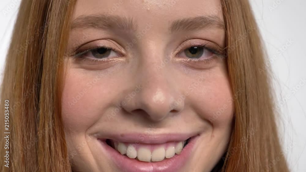 Face of young sweet calm ginger girl is watching at camera, smiling, white background Face of young sweet calm ginger girl is watching at camera, smiling, white background