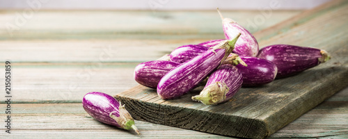 Heap of small eggplant or aubergine vegetable on old wooden background. Healthy food concept with copy space. Banner.