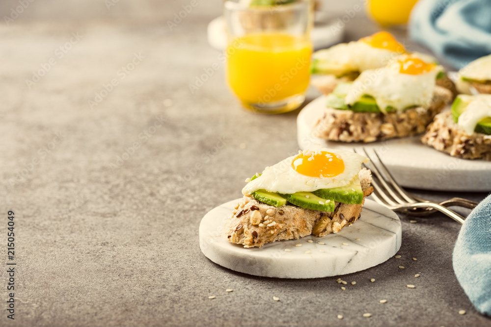 Healthy sandwich with fresh avocado and fried quail egg on small marble board on gray background. Breakfast or lunch food concept with copy space. Retro style toned.