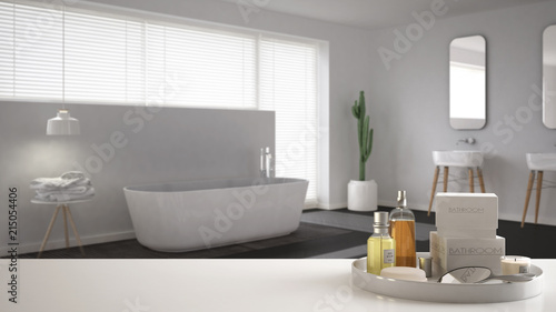 Spa, hotel bathroom concept. White table top or shelf with bathing accessories, toiletries, over blurred minimalist bathroom, modern architecture interior design