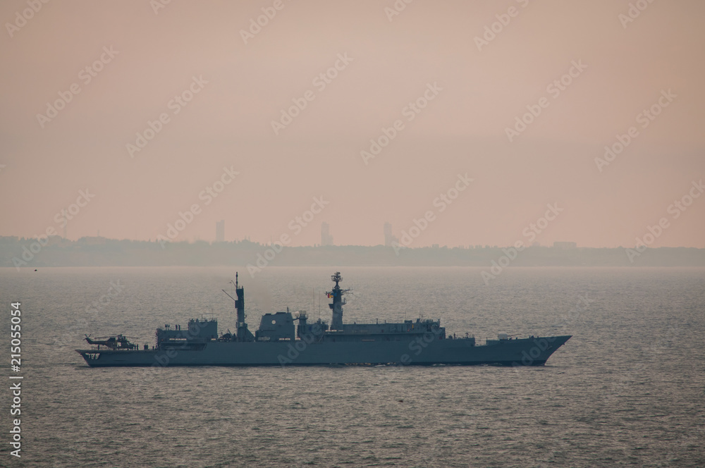 Military ship naval forces  sailing in the Black sea with buildings and a plant on the background. Military training. Gloomy foggy morning