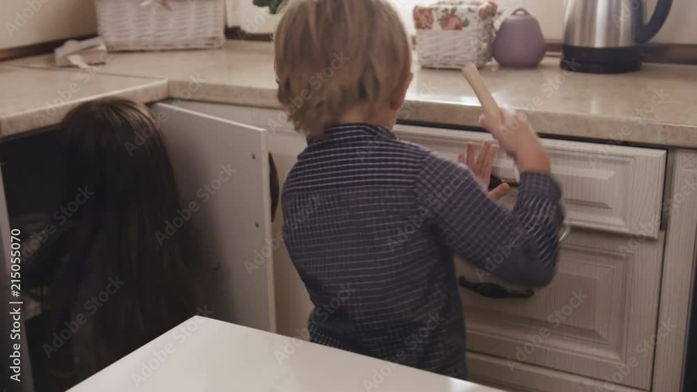 Two little kids running into the cozy kitchen and starting to pull out all kitchen stuff for cooking. Inside Two little kids running into the cozy kitchen and starting to pull out all kitchen stuff for cooking. Inside