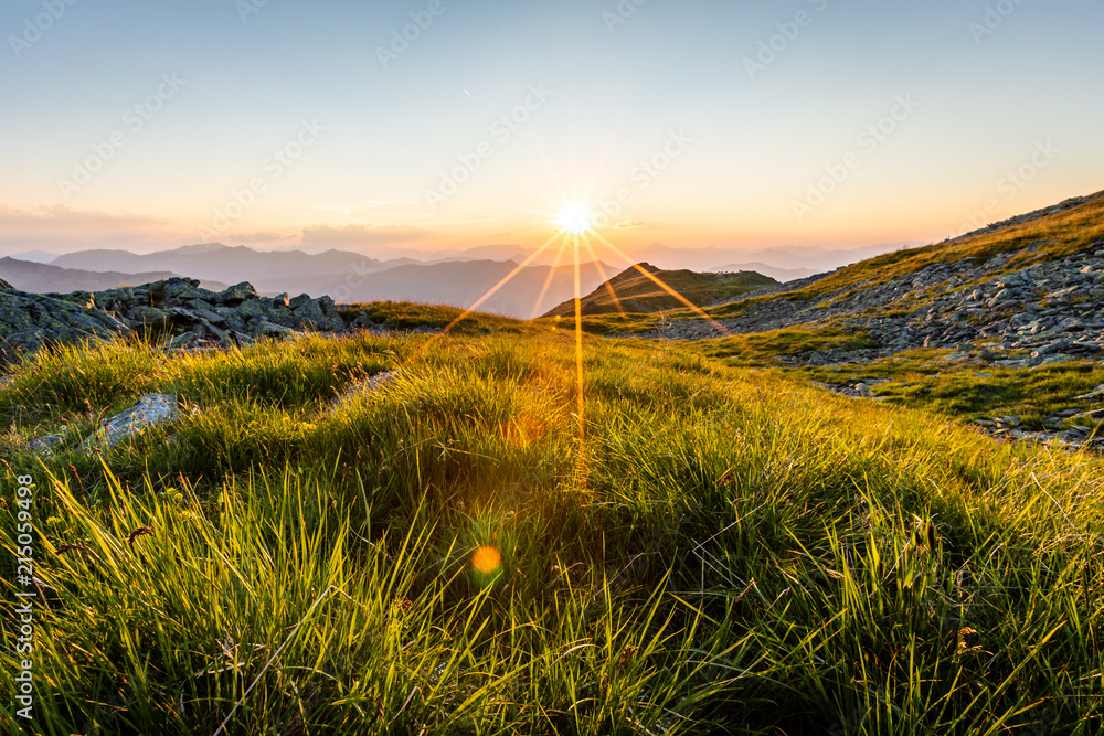 Fototapeta premium Sonnenuntergang am Berg mit Gras im Vordergrund