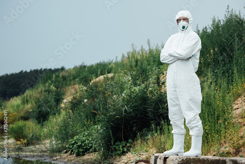 male scientist in protective suit and mask standing near water outdoors