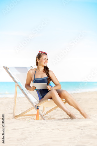woman looking into the distance and using tablet PC while sitting in a beach chair