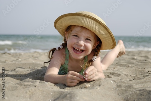 Little girl lies at a sandy beach at the sea
