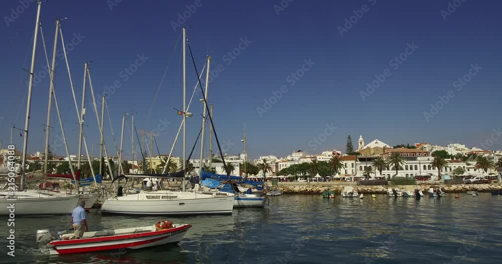 City pier with sailing yachts and fishing boats, parking of fishing boats in the city port of Lagos ,Portugal, Against the backdrop of a seaside town of Lagos in Algarve. Small boat pass on going out. City pier with sailing yachts and fishing boats, parking of fishing boats in the city port of Lagos ,Portugal, Against the backdrop of a seaside town of Lagos in Algarve. Small boat pass on going out.