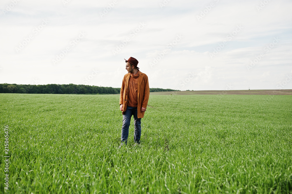 Stylish man in glasses, brown jacket and hat posed on green field. Stylish man in glasses, brown jacket and hat posed on green field.