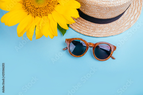 Fotografie Fashion flatlay with sunglasses, straw boater hat and bright big yellow sunflower on blue background