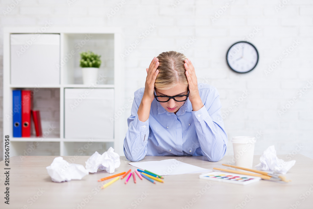 creativity and idea crisis - thoughtful girl with paint brushes, colorful pencils and crumpled papers