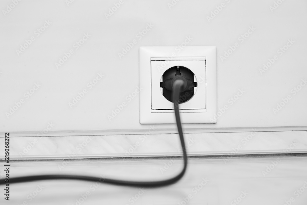Electric white socket and one plugged in power cord on white wall background Electric white socket and one plugged in power cord on white wall background