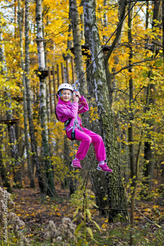Young girl on zip line between trees in an adventure park.