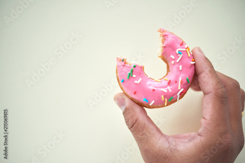 Crop person holding pink glazed doughnut in colorful sprinkles and with bite taken out against white background