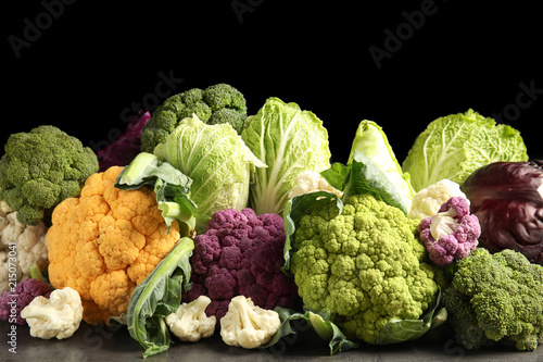 Different fresh cabbages on table against black background. Healthy food