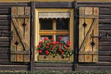 drewniany stary dom z drewnianymi okiennicami i czerwonymi pelargoniami w skrzynce