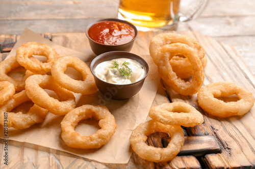 Fried onion rings served with sauces on wooden board, closeup