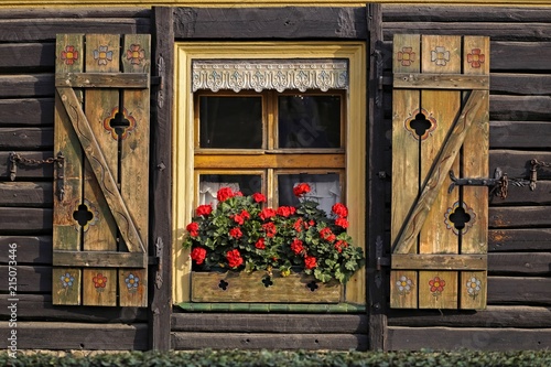 drewniany stary dom z drewnianymi okiennicami i czerwonymi pelargoniami w skrzynce