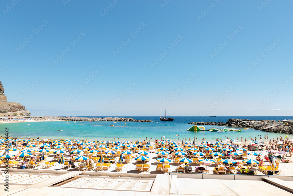 Las Americas, Canarias islands/ Spain-July 22, 2018: View of beach fool of tourists and umbrellas for sun on Canarias, view of bay with mountains. Blue Atlantic ocean and beach on Gran Canaria.