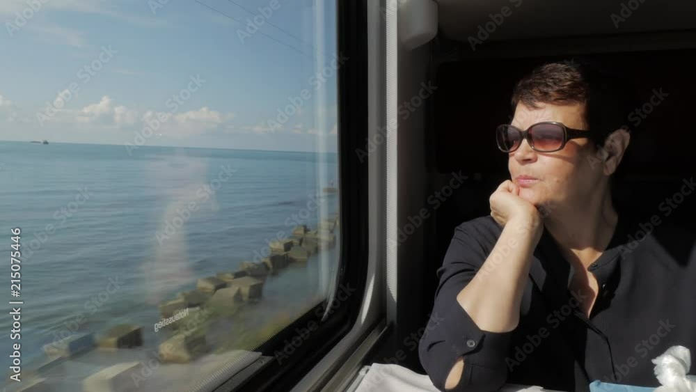 Attractive elderly woman in sunglasses sitting near window in train cabin, looking at bright sunny sea view and talking. 4K Attractive elderly woman in sunglasses sitting near window in train cabin, looking at bright sunny sea view and talking. 4K