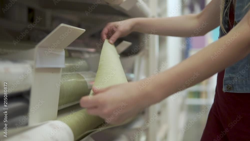 Female hands are touching wallpaper in a building materials store. Buyer is checking quality of paper, close-up of hands Female hands are touching wallpaper in a building materials store. Buyer is checking quality of paper, close-up of hands
