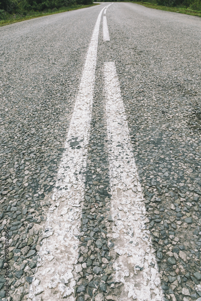 Highway of tiny asphalt gravel close up. Background of rough asphalt road of granular stones with white road marking in perspective. Detailed grunge texture with bokeh. Rural route with copy space.