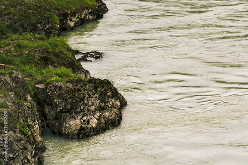 Gloomy view from above on rocky sinuous riverbank. Dark green of water. Eerie atmosphere in overcast rainy weather in cinematic faded tones. Landscape with shore of river in horror style.