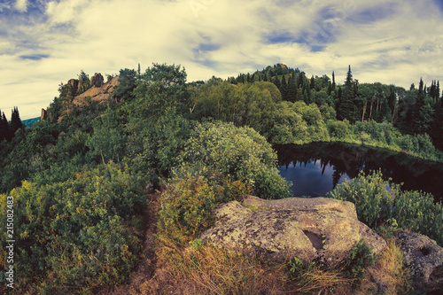 Lake on top of hill  surrounded by rocks and thickets  captured by the fisheye lens.