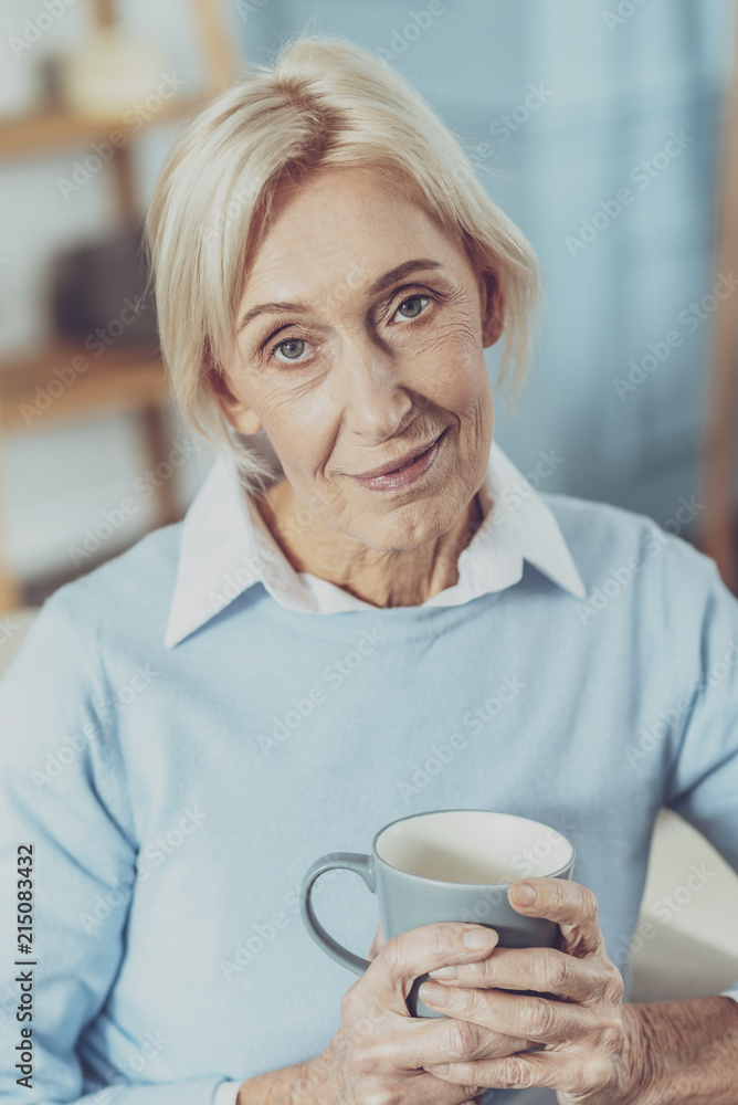 Look at me. Charming pensioner holding cup in both hands and keeping smile on face Look at me. Charming pensioner holding cup in both hands and keeping smile on face