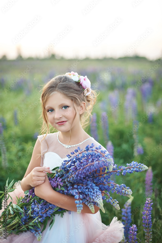 Fototapeta premium Beautiful girl in pink dress holding a lupine at sunset on the field. The concept of nature and romance. Happy childhood