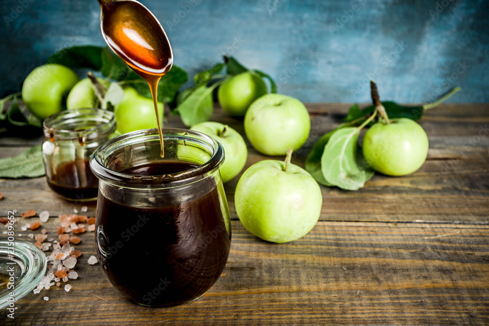 Home cooked dark salted classic caramel sauce, with green apples, wooden and dark blue background, Home cooked dark salted classic caramel sauce, with green apples, wooden and dark blue background,