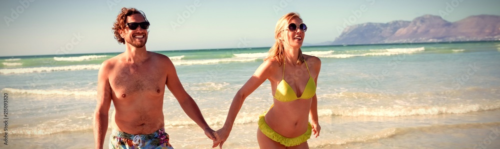 Happy young couple holding hands while running at beach Happy young couple holding hands while running at beach
