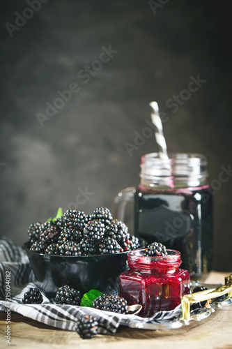 Ripe blackberry, blackberry juice and jam on a wooden table. Dark background.