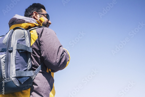 middle age man caucasian viewed from back side with backpack. trekking and enjoying the hike leisure activity outdoor in the nature. clear blue sky in background, smile and happiness concept photo