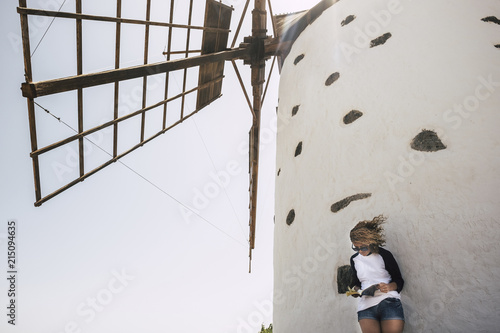 nice beautiful cheerful lady with blonde curly hair standing under a windmill in outdoor scenic place reading a book and enjoying the leisure activity.  happy lifestyle concept  photo