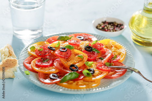 Blue plate with homemade tomato carpaccio on blue table with bread and water.