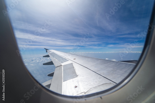 Wing of airplane flying above the clouds in the blue sky background through the window.