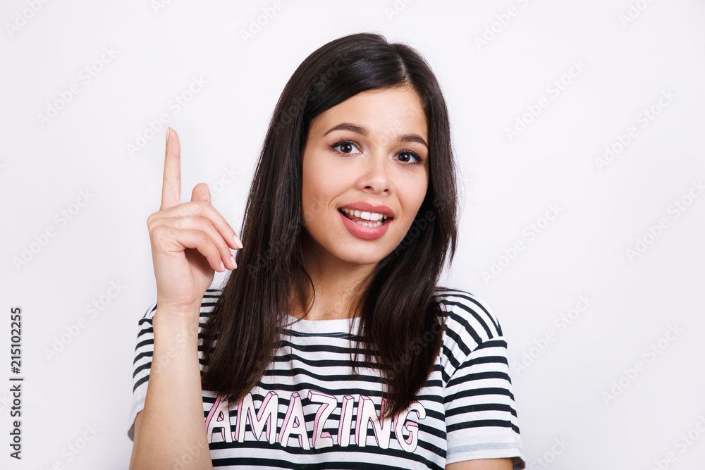 Good looking brunette female with pure healthy skin looks in amazement as indicates at something upwards Good looking brunette female with pure healthy skin looks in amazement as indicates at something upwards